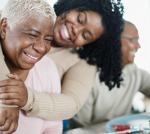 African daughter hugging her mum during lunch meal at home - Love and family concept - Main focus on senior woman face